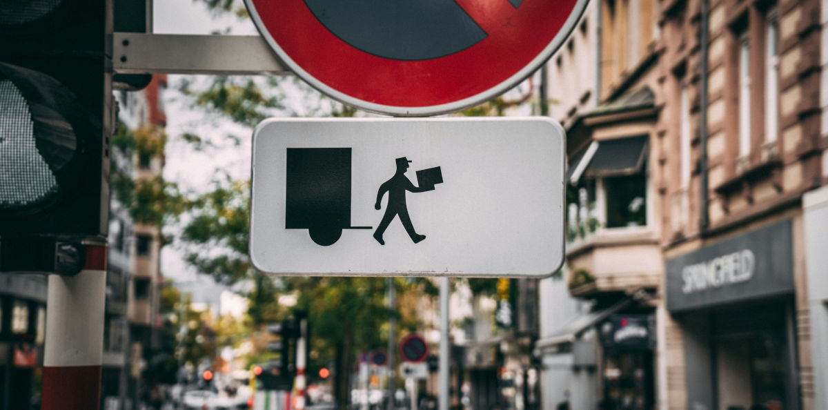 Photo by Mika Baumeister on Unsplash - https://unsplash.com/photos/red-and-white-stop-sign-WOn90Iui_08 A street sign showing a man carrying a delivery package